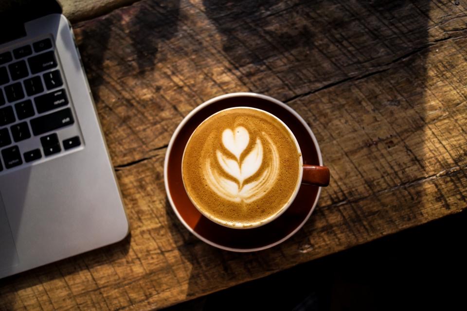 A laptop on a desk next to a cup of coffee